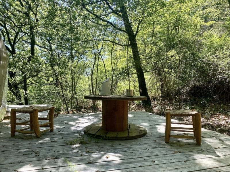 Tente de glamping avec une terrasse en bois entourée darbres verdoyants.