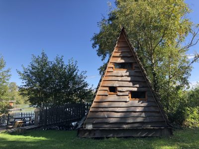 Cabane en bois en forme de pyramide, entourée darbres verdoyants à Auvergne-Rhône-Alpes.