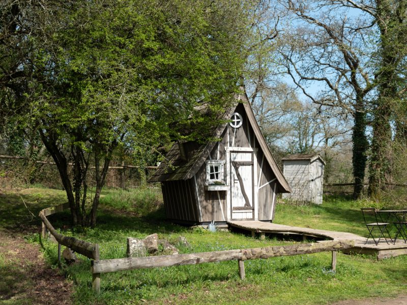 Cabane en bois atypique en Bretagne, entourée de verdure et darbres.