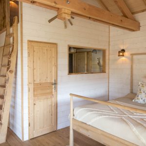 Cabane en bois en Bretagne, intérieur lumineux avec lit douillet et échelle en bois.