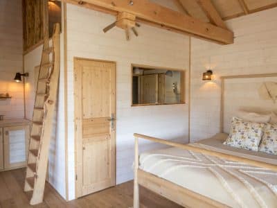 Cabane en bois en Bretagne, intérieur lumineux avec lit douillet et échelle en bois.