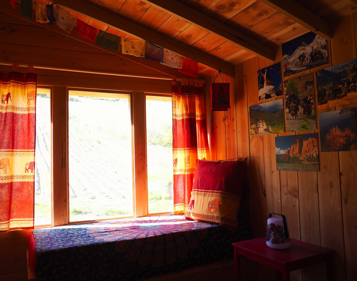 Cabane en bois chaleureuse avec coussins colorés et vue sur la nature.