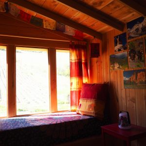 Cabane en bois chaleureuse avec coussins colorés et vue sur la nature.