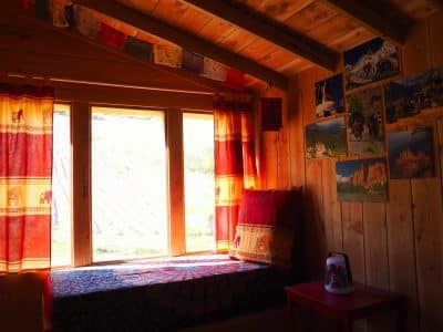 Cabane en bois chaleureuse avec coussins colorés et vue sur la nature.