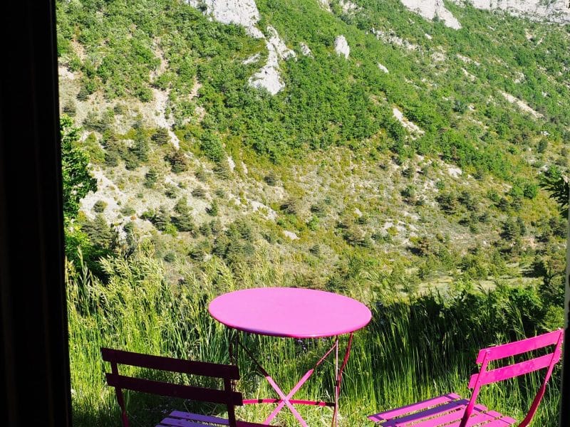 Chalet avec vue imprenable, table et chaises roses sur la terrasse verdoyante.
