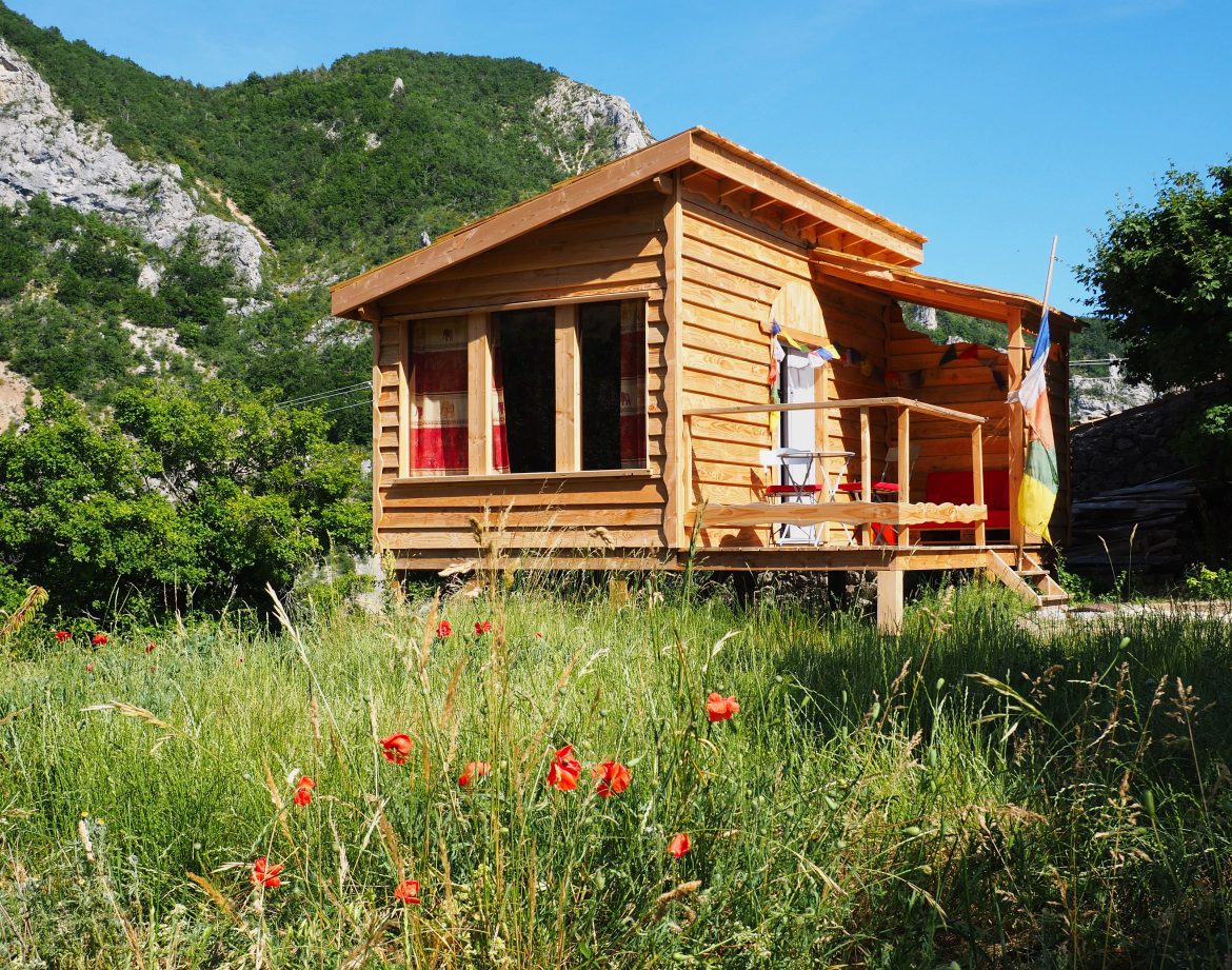 Cabane en bois au cœur de la nature, entourée de fleurs sauvages et montagnes.