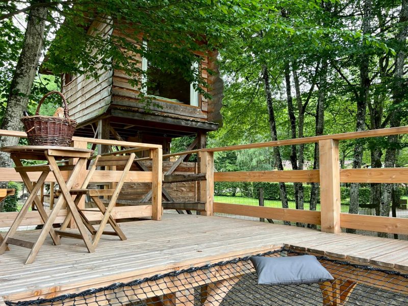 Cabane perchée en bois avec terrasse en bois et vue sur la nature verdoyante.
