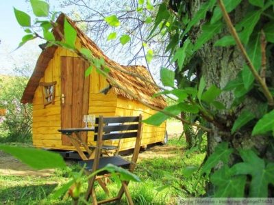Cabane en bois à Auvergne, entourée de verdure, avec une terrasse et des chaises.