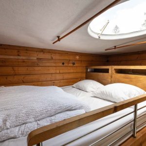 Chalet en bois cosy avec lit double et fenêtre ronde pour admirer les étoiles.