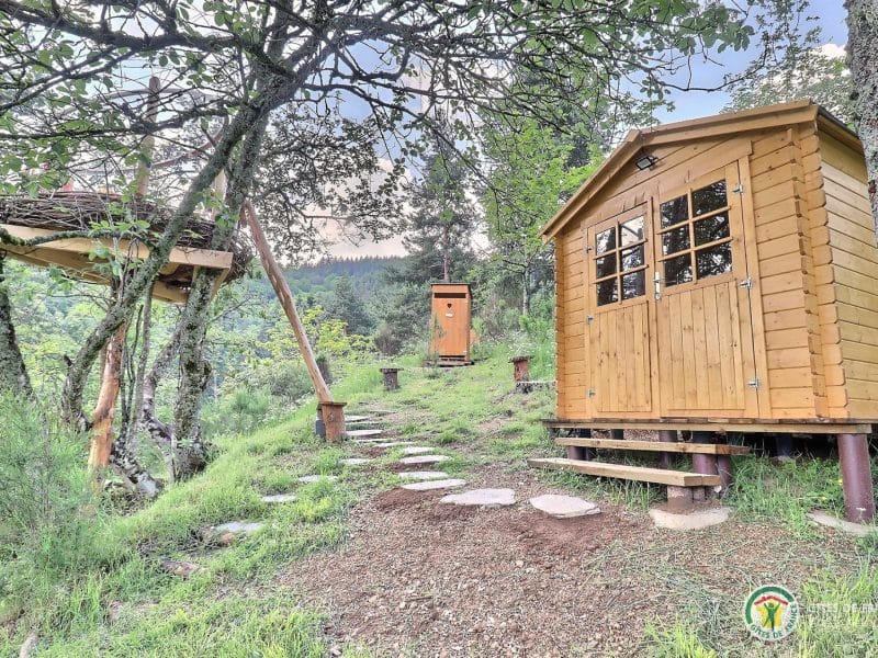 Cabane en bois entourée darbres, avec un chemin de pierres menant à lentrée.