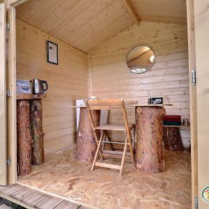 Cabane en bois cosy avec table en troncs et miroir rond, idéale pour un séjour nature.