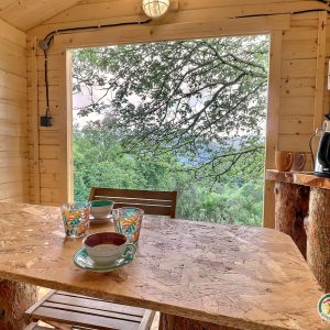 Cabane en bois avec vue sur la nature, table en bois et tasses colorées.