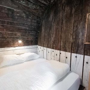Cabane en bois dans les Ardennes, avec un lit douillet et une fenêtre sur la nature.