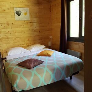 Chalet en bois à Champagne-Ardennes, chambre cosy avec lit double et décor chaleureux.