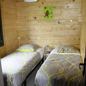 Chalet en bois à Champagne-Ardenne avec deux lits simples et une décoration chaleureuse.