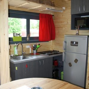 Cabane en bois à Champagne-Ardenne, cuisine moderne avec rideau rouge et vue sur la nature.