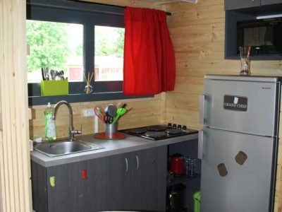 Cabane en bois à Champagne-Ardenne, cuisine moderne avec rideau rouge et vue sur la nature.