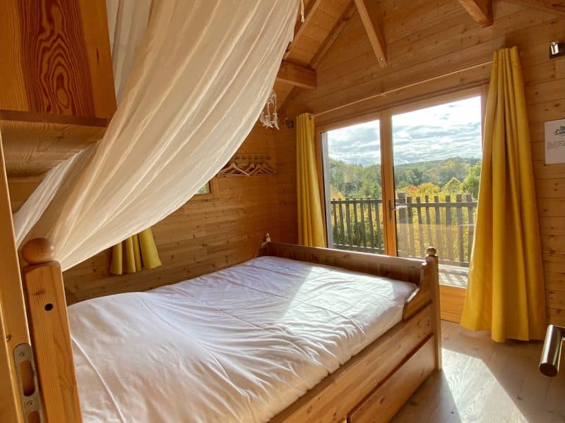 Chalet en bois avec lit confortable et vue sur la nature à travers de grandes fenêtres.