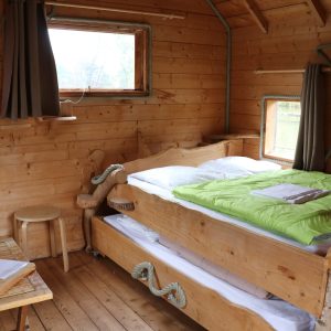 Cabane en bois dans les arbres, lit douillet avec draps verts et vue sur la nature.