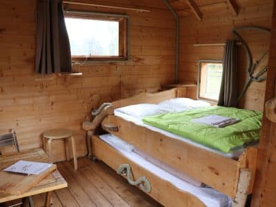Cabane en bois dans les arbres, lit douillet avec draps verts et vue sur la nature.