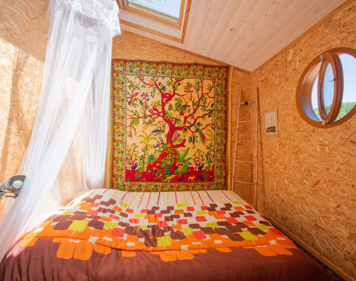 Chalet en bois avec lit douillet et tapisserie colorée, lumineux et accueillant.