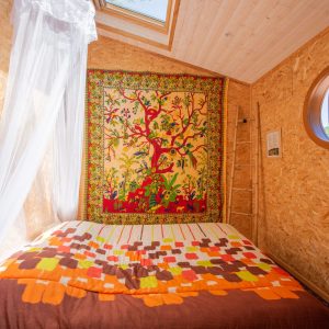 Chalet en bois avec lit douillet et tapisserie colorée, lumineux et accueillant.
