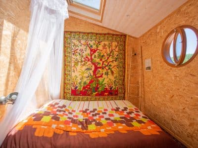 Chalet en bois avec lit douillet et tapisserie colorée, lumineux et accueillant.