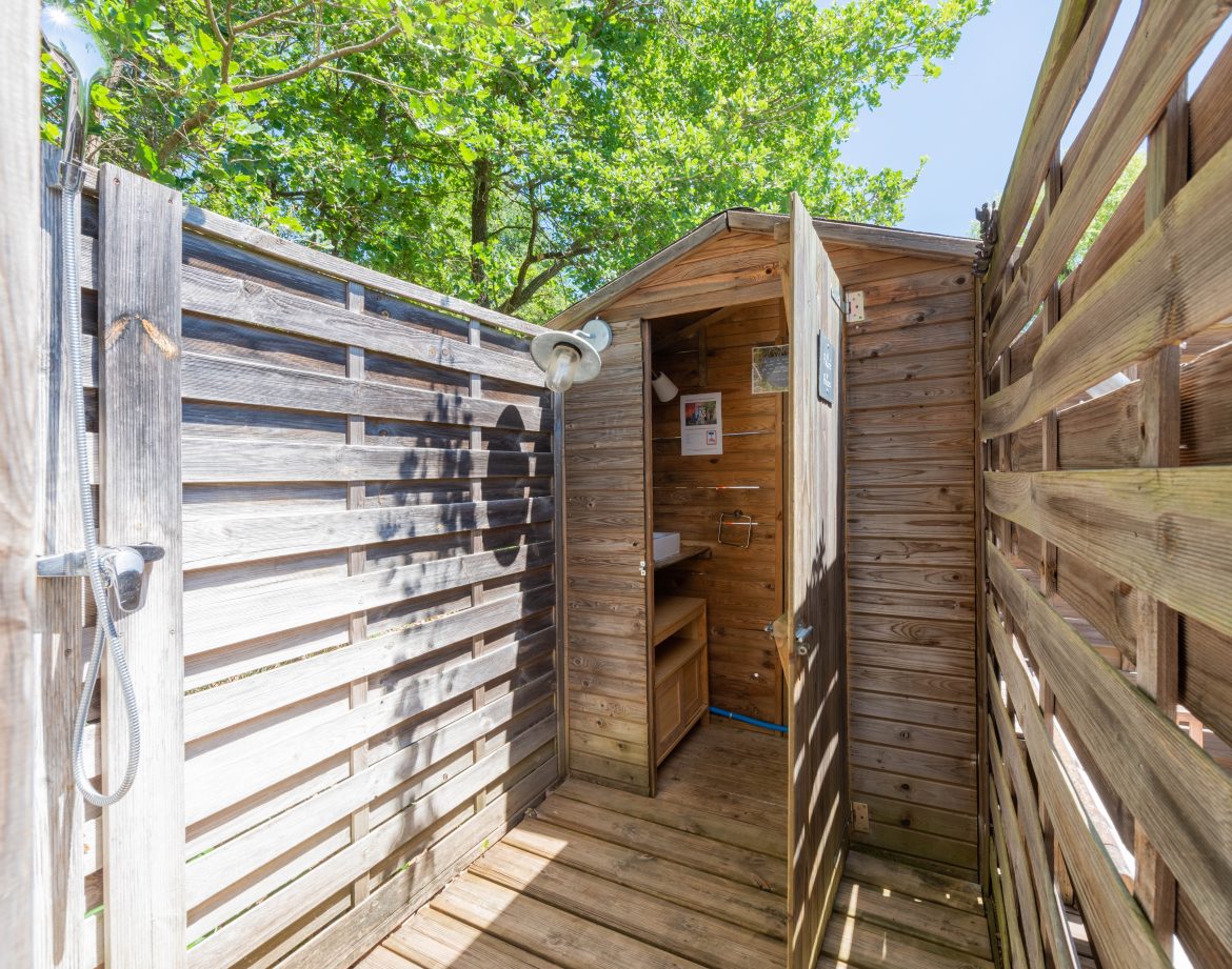 Cabane en bois avec douche extérieure, entourée de verdure à Languedoc-Roussillon.