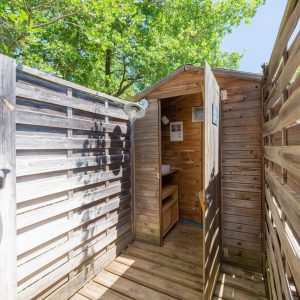 Cabane en bois avec douche extérieure, entourée de verdure à Languedoc-Roussillon.