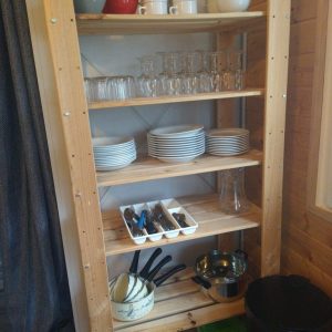 Étagère en bois dans un hébergement insolite, avec vaisselle colorée et ustensiles de cuisine.