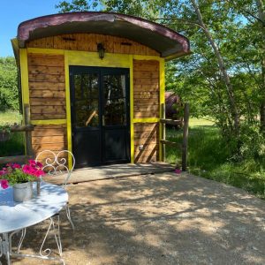 Charmante roulotte en bois avec une terrasse fleurie, située en pleine nature en Auvergne.