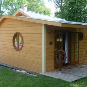 Cabane en bois avec un grand hublot et un baromètre, idéale pour un séjour insolite.