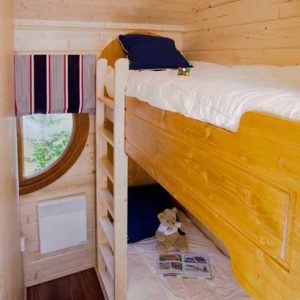 Cabane en bois avec lits superposés et fenêtre ronde, idéale pour un séjour insolite.