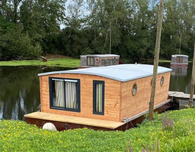 Cabane flottante en bois au bord dun étang, entourée de fleurs sauvages.