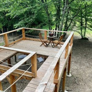 Cabane perchée en bois avec terrasse et mobilier en plein air, entourée darbres.
