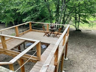 Cabane perchée en bois avec terrasse et mobilier en plein air, entourée darbres.