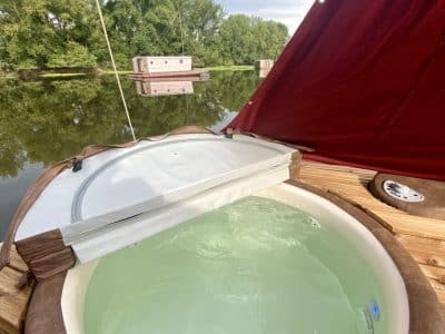 Hébergement insolite en Auvergne : un bateau avec jacuzzi sur leau paisible.