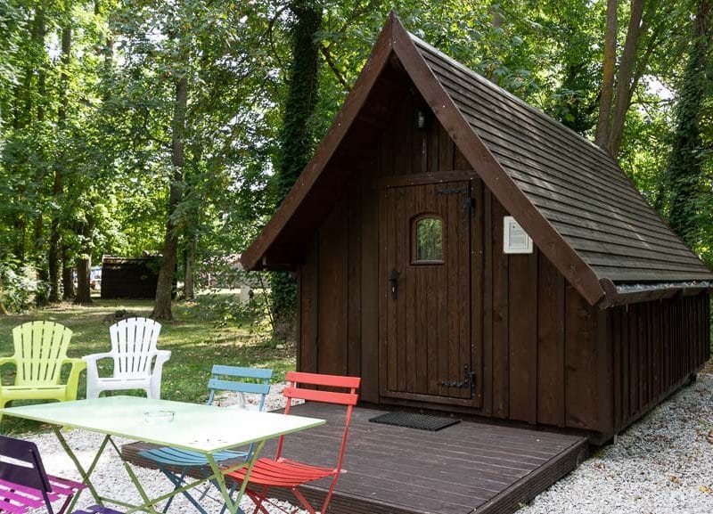 Cabane en bois à Champagne-Ardenne, entourée de verdure et de mobilier coloré.