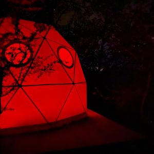 Dôme géodésique illuminé en rouge, niché dans la nature du Languedoc-Roussillon.