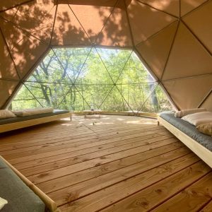 Dôme géodésique en bois, intérieur lumineux avec lits confortables et vue sur la nature.