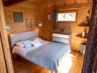 Chalet en bois lumineux en Bretagne, avec un lit douillet et des murs en bois chaleureux.