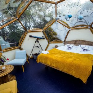 Dôme transparent en Bretagne, lit douillet avec couverture jaune et vue sur la nature.