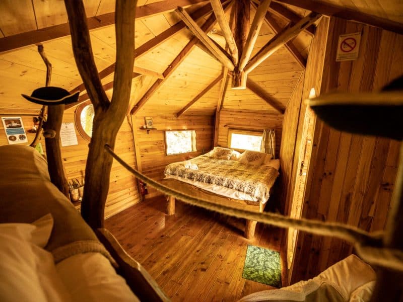 Cabane en bois en Bretagne, intérieur chaleureux avec lit douillet et murs en bois.