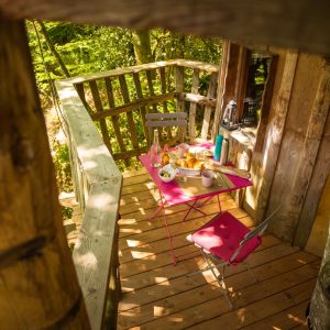 Cabane perchée en Bretagne avec une terrasse en bois et une table colorée.
