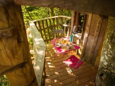 Cabane perchée en Bretagne avec une terrasse en bois et une table colorée.