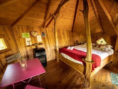 Cabane en bois en Bretagne, intérieur chaleureux avec lit douillet et table rose.