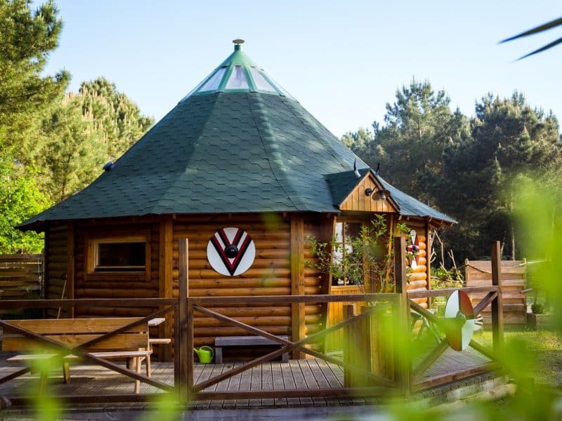 Cabane en bois ronde en Bretagne, avec un toit vert et une terrasse en bois.