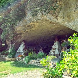 Tipis en pierre sous une falaise, entourés de verdure et de fleurs colorées.