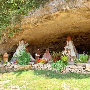 Tentes de style amérindien sous une grotte, entourées de fleurs colorées.