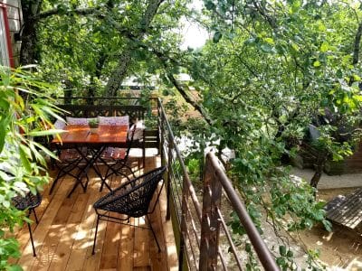 Cabane perchée dans les arbres, avec terrasse en bois et chaises noires.